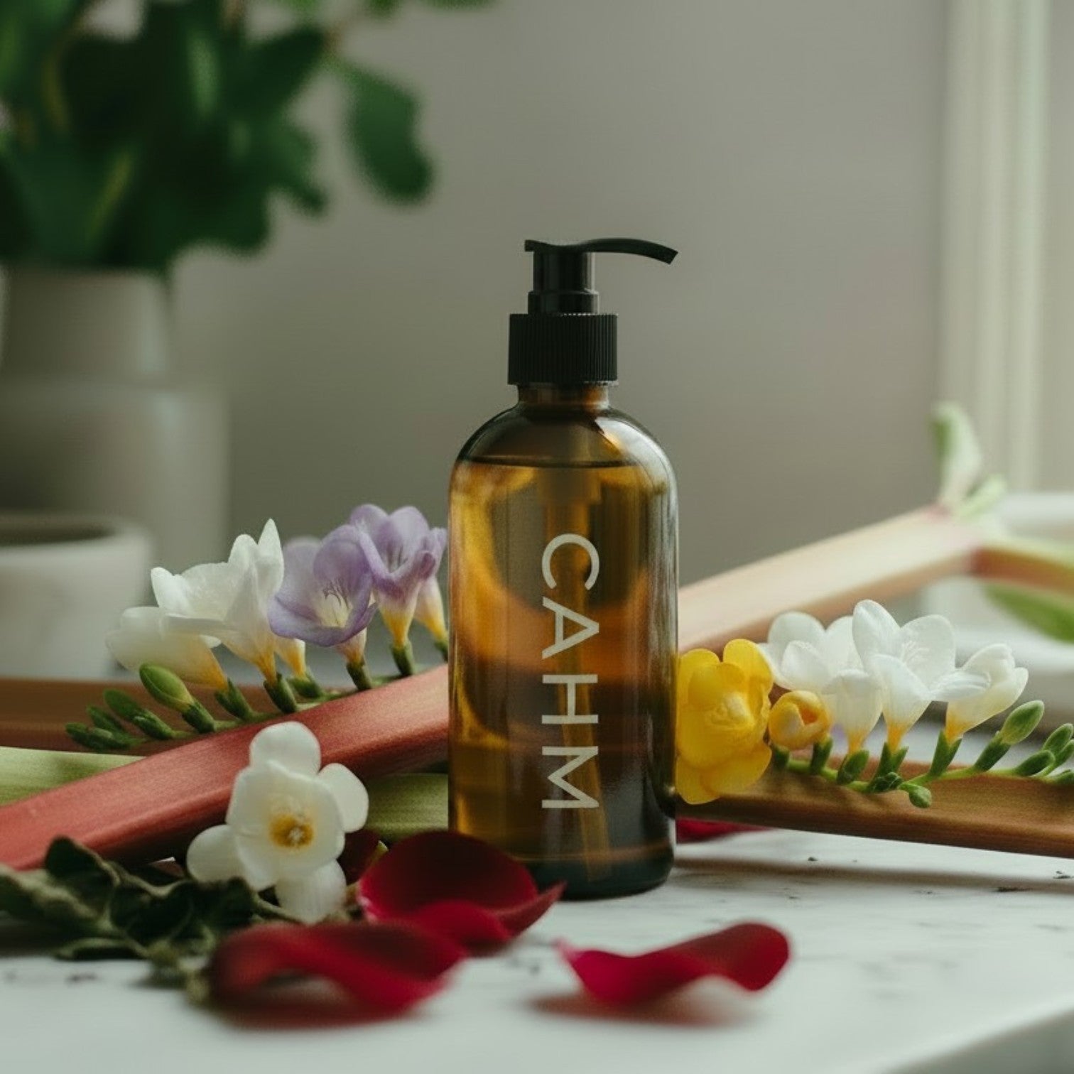 Brown bottle with black pump labeled 'CAHM' surrounded by flowers on a marble surface.