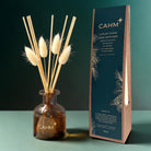 CAHM Luxury Home Reed Diffuser set featuring an amber glass bottle with dried bunny tail reeds, next to its dark teal and kraft paper packaging box.