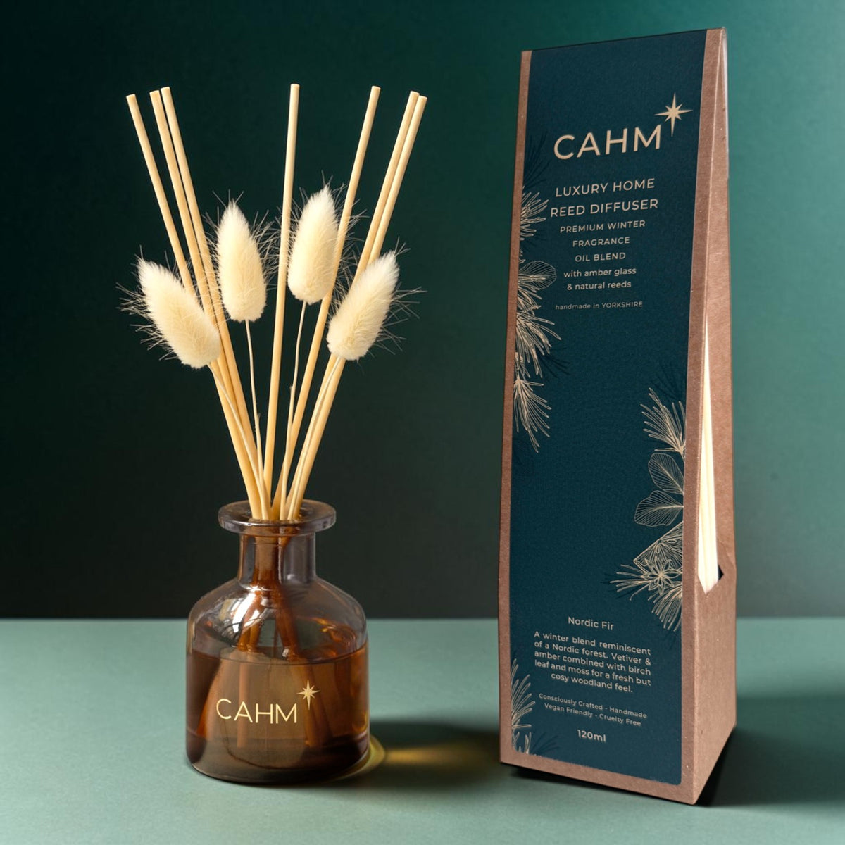 CAHM Luxury Home Reed Diffuser set featuring an amber glass bottle with dried bunny tail reeds, next to its dark teal and kraft paper packaging box.